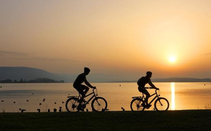 2 cyclists biking along the lake, reference to youth camp of the JAB (Jeunesse Action Biblique).