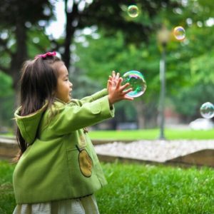 fille qui joue dehors avec une bulle de savon, affiche pour les rendez vous pour les activités enfants à Renens-Lausanne KidsTeam , summer camp kids team Lausanne / Vaud, girl playing outside catching a soap bubble