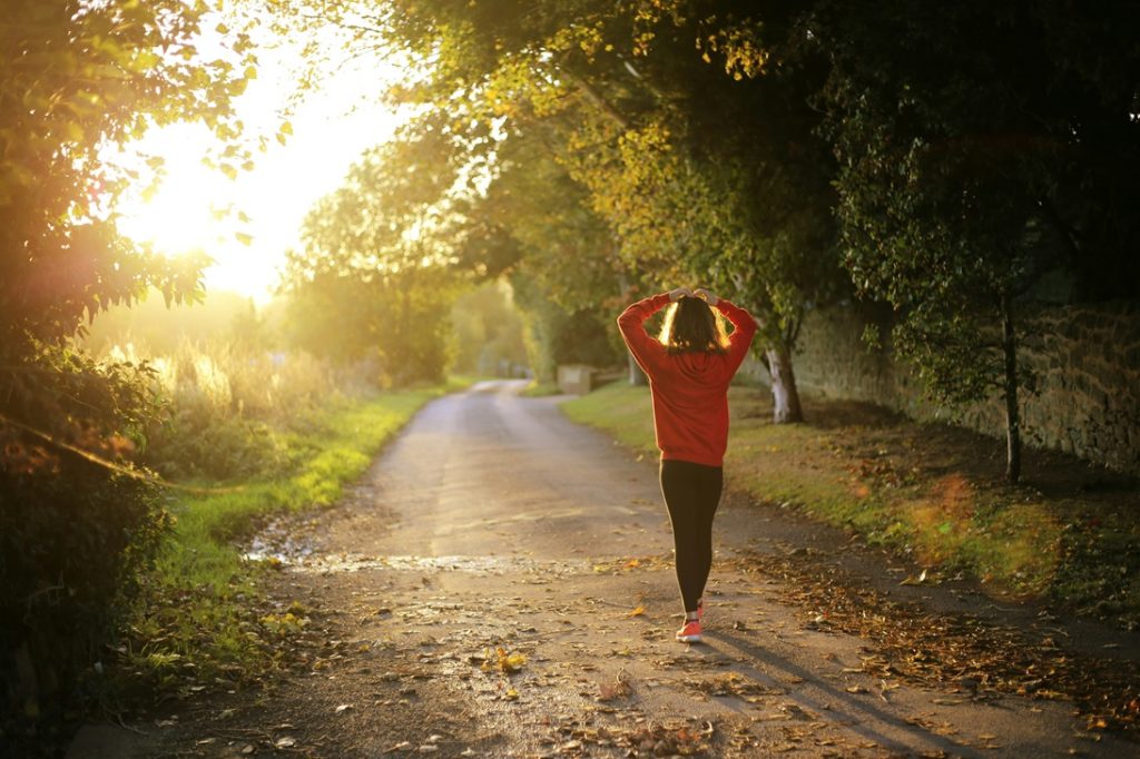 coureuse de marathon pendant un entraînement dans la forêt. Long chemin devant elle et soleil au fond de l'image.