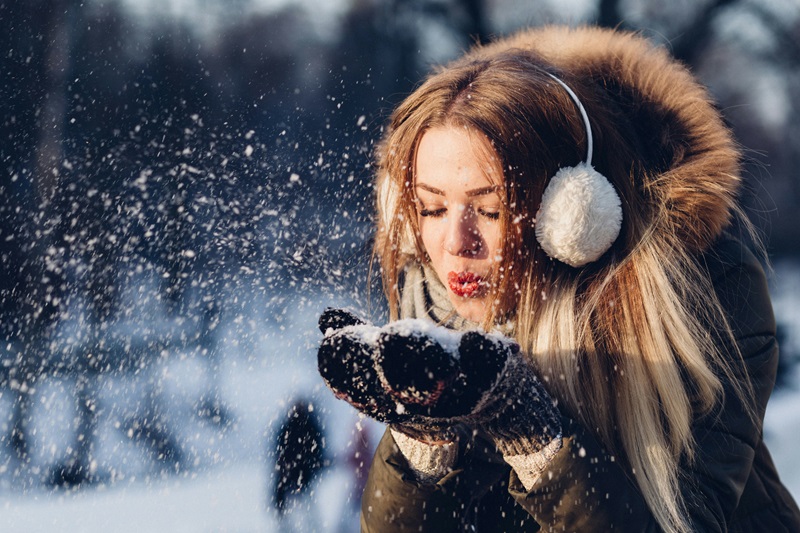 girl warmly dressed blowing snow in her hands